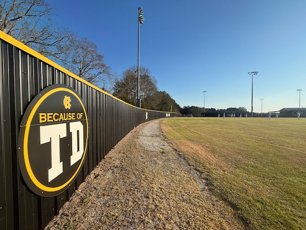 Harris County baseball's slogan, "Because of TD," honors late coach Tony Dimitri, who died Jan. 24. The slogan is displayed on the outfield wall behind center field and right field. (Jack Leo/AJC)