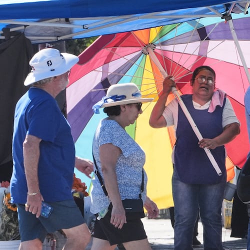 A street vendor uses an umbrella to shelter from the sun on a unseasonably hot day Tuesday, Oct. 28, 2025, in Los Angeles. (AP Photo/Damian Dovarganes)