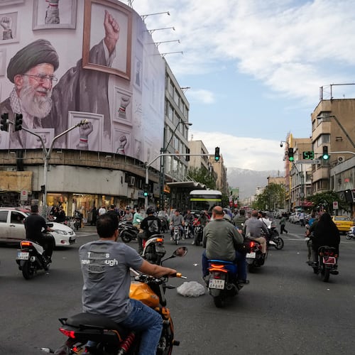 Motorbikes drive past a billboard with graphic showing the late Iranian Supreme Leader Ayatollah Ali Khamenei, who was killed in the U.S. and Israel strikes on Feb. 28, with his framed fist amongst his supporters framed fists in downtown Tehran, Iran, Wednesday, May 6, 2026. (AP Photo/Vahid Salemi)