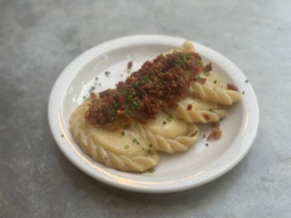 4 Plated house pierogi topped with bacon on white plate.