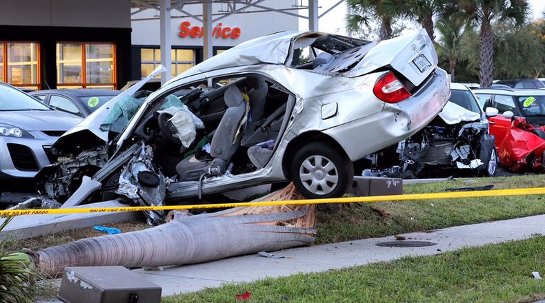 A car sits atop a light pole and palm tree after crashing into cars parked adjacent to US 1 at Delray Mazda Tuesday morning, August 25, 2015.  (Lannis Waters / The Palm Beach Post)