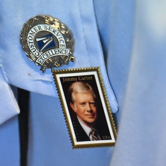 Jessica Stevens of the U.S. Postal Service wears a pin of the newly released "forever" stamp of former President Jimmy Carter at the nonprofit Carter Center in Atlanta on Wednesday. Carter, who died last December, would have turned 101 on Wednesday. (Hyosub Shin/AJC)