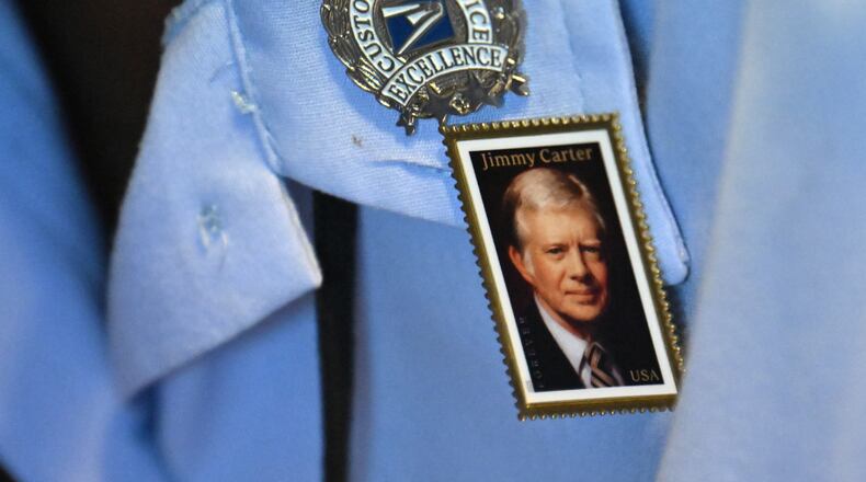 Jessica Stevens of the U.S. Postal Service wears a pin of the newly released "forever" stamp of former President Jimmy Carter at the nonprofit Carter Center in Atlanta on Wednesday. Carter, who died last December, would have turned 101 on Wednesday. (Hyosub Shin/AJC)