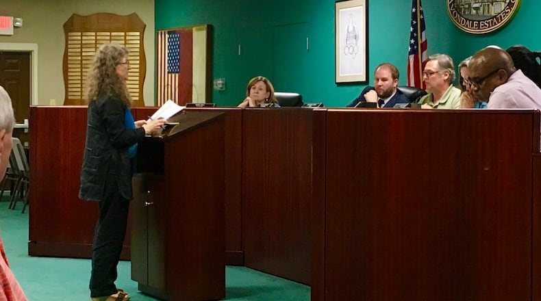 Avondale Estates resident Liz Goodstein reading her statement before the Board of Mayor Commissioners and City Manager Patrick Bryant (in suit) with Mayor Jonathan Elmore (to Bryant’s left). Goodstein, who opposes creating a URA and issuing a bond anticipation note, had written, “… it should be troubling to every citizen that our BOMC is contemplating empowering itself to issue millions in bonds, a decision that will have consequences for decades, without consulting with the voters who will pay the bills.” She also told commissioners on this night that they were taking “steps … outside the proper democratic process.” Bill Banks for the AJC