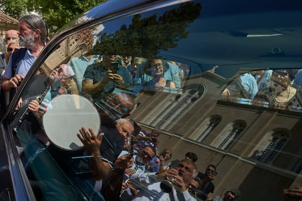 Musicians are reflected in a window of a hearse with the coffin of renowned clarinetist Petroloukas Chalkias, who died at 90 over the weekend, during a farewell ceremony at Athens Cathedral on Wednesday, June 18, 2025. (AP Photo/Petros Giannakouris)