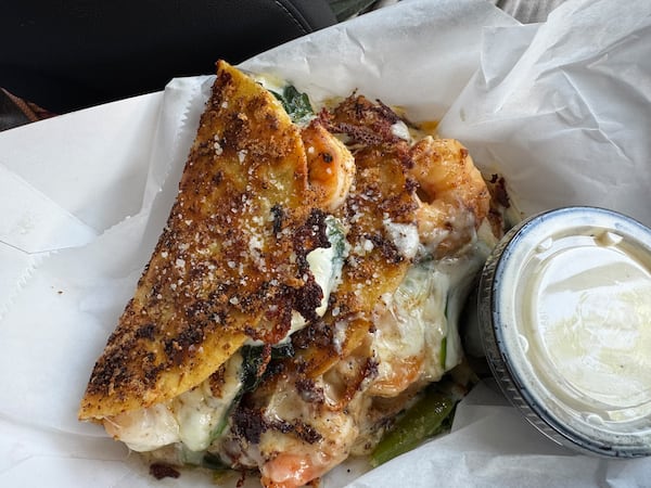 A takeaway plate with two griddled tacos served with a creamy sauce on the side