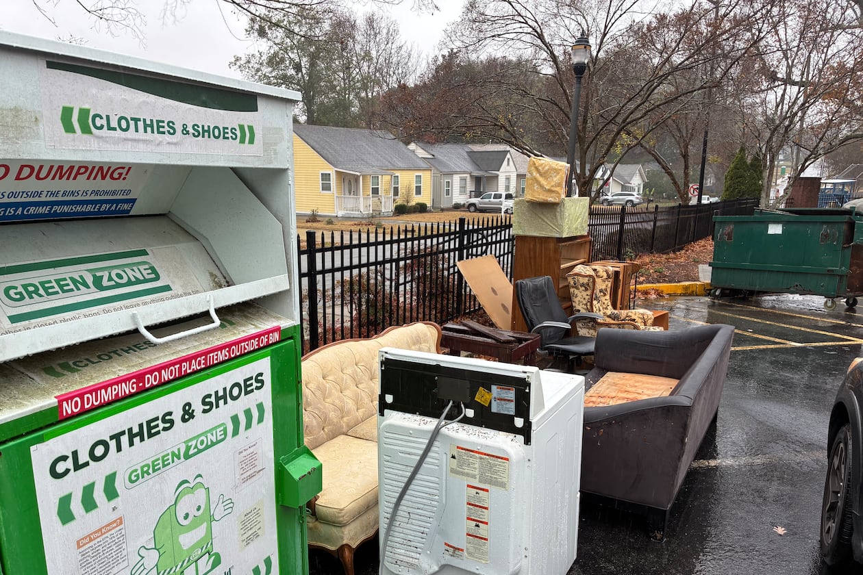 A bin for the textile reclamation company Green Zone LLC has become a dumping spot for discarded furniture and other trash in the parking lot of a skilled nursing facility on Temple Avenue in College Park. (Nedra Rhone/AJC)
