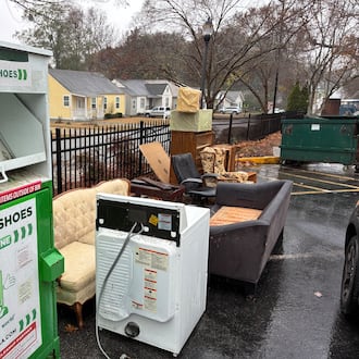 A bin for the textile reclamation company Green Zone LLC has become a dumping spot for discarded furniture and other trash in the parking lot of a skilled nursing facility on Temple Avenue in College Park. (Nedra Rhone/AJC)