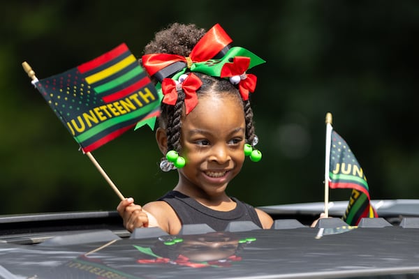 Gigi Chism, 4, waves flags from a car during the Juneteenth parade in College Park on Thursday, June 19, 2025. (Arvin Temkar/AJC)