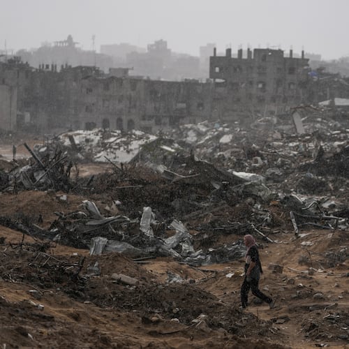 A Palestinian woman walks through a rainstorm past buildings destroyed in Israeli strikes in the Sheikh Radwan neighborhood of Gaza City, Friday, Nov. 14, 2025. (AP Photo/Jehad Alshrafi)