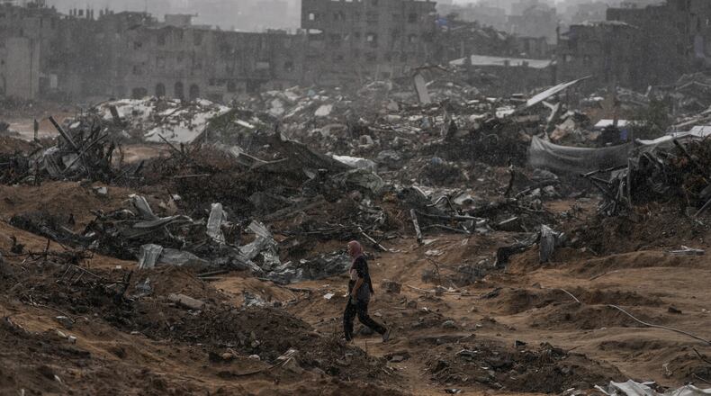 A Palestinian woman walks through a rainstorm past buildings destroyed in Israeli strikes in the Sheikh Radwan neighborhood of Gaza City, Friday, Nov. 14, 2025. (AP Photo/Jehad Alshrafi)