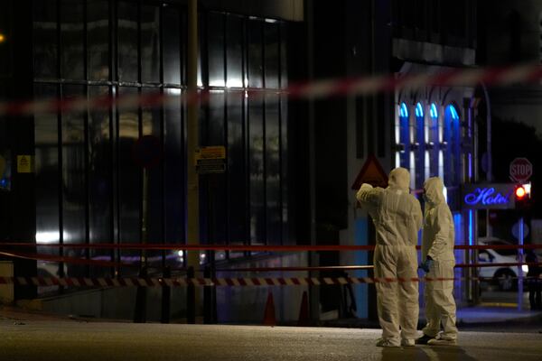 Police investigators wearing coveralls inspect the site after a bomb explosion outside of the Hellenic Train offices the company that runs Greece's railway, the first building on the left, in Athens, Greece, Friday, April 11, 2025. (AP Photo/Petros Giannakouris)