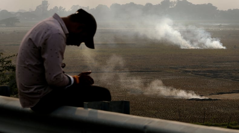 FILE - A person checks his mobile phone as farmers burn crop residue after harvest near Bundelkhand expressway in India, on Nov. 17, 2024. (AP Photo/Manish Swarup, File)