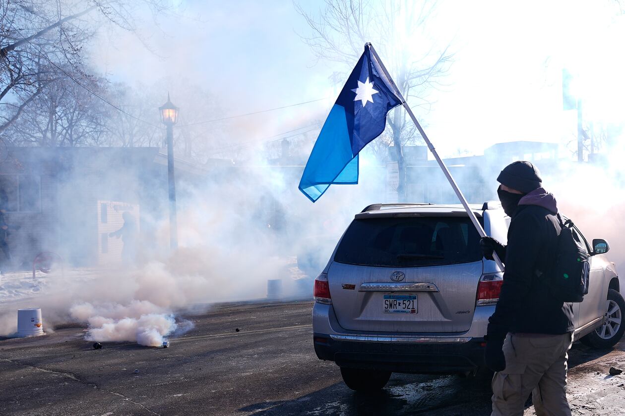A person holds a Minnesota state flag as federal immigration officers deploy tear gas Saturday, Jan. 24, 2026, in Minneapolis. (AP Photo/Abbie Parr)