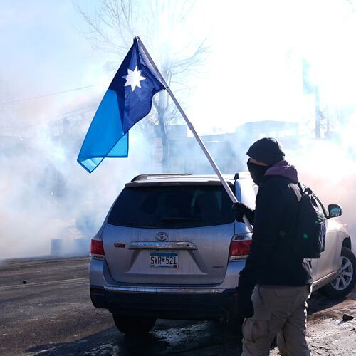 A person holds a Minnesota state flag as federal immigration officers deploy tear gas Saturday, Jan. 24, 2026, in Minneapolis. (AP Photo/Abbie Parr)