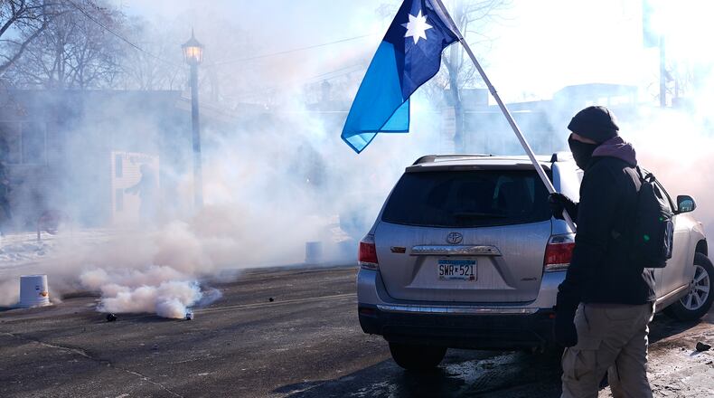 A person holds a Minnesota state flag as federal immigration officers deploy tear gas Saturday, Jan. 24, 2026, in Minneapolis. (AP Photo/Abbie Parr)