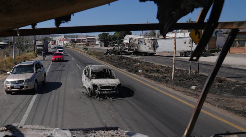 Vehicles pass a burned car a day after the Mexican army killed Jalisco New Generation Cartel leader Nemesio Oseguera Cervantes, known as "El Mencho," in Guadalajara, Mexico, Monday, Feb. 23, 2026. (AP Photo/Marco Ugarte)