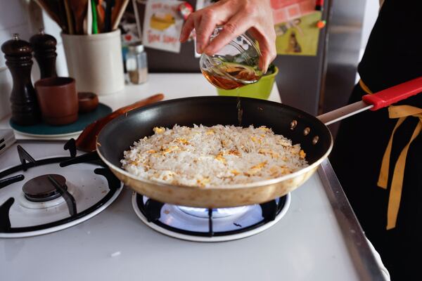 Lazy Betty executive chef Ron Hsu adds oil to his collard green fried rice at his home in Atlanta on Wednesday, Feb. 18, 2026. The recipe is one of the many featured in his new cookbook “Down South + East.”(Natrice Miller/AJC)