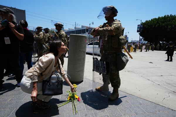 A woman lays flowers in front of a National Guard as protesters gather to denounce ICE, U.S Immigration and Customs Enforcement, operations Tuesday, June 10, 2025, in Los Angeles. (AP Photo Damian Dovarganes)