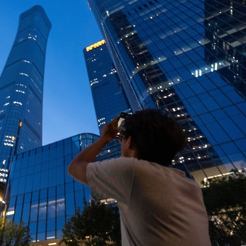 A passerby tries to take photo of the damage on the Citic Tower also known as Zun Tower in Beijing, China, Friday, June 26, 2026. (AP Photo/Han Guan Ng)