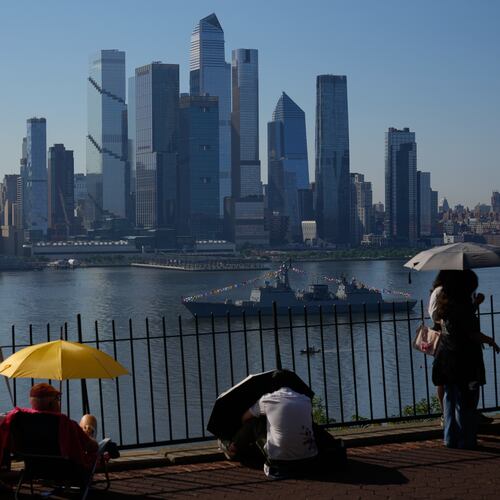 People take cover from the heat under umbrellas as they wait for a parade of tall ships and flyovers in Weehawken, N.J., Saturday, July 4, 2026. (AP Photo/Seth Wenig)