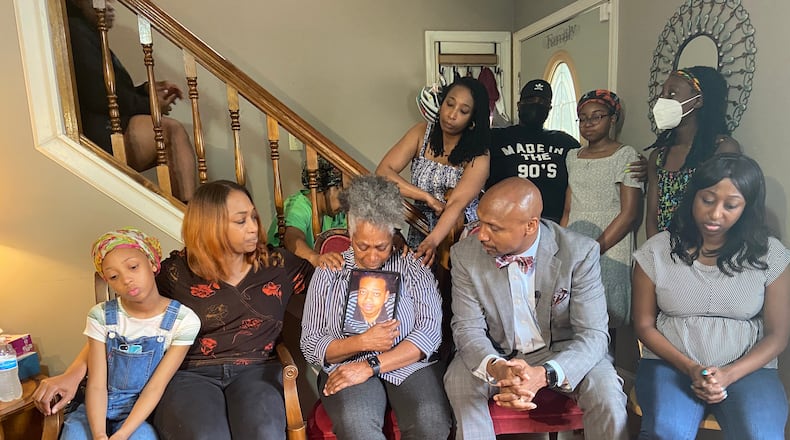 Matthew Williams' mother holds up his photo as she is consoled by family members in her living room. Williams was killed during an encounter with police Monday at his DeKalb County condo.