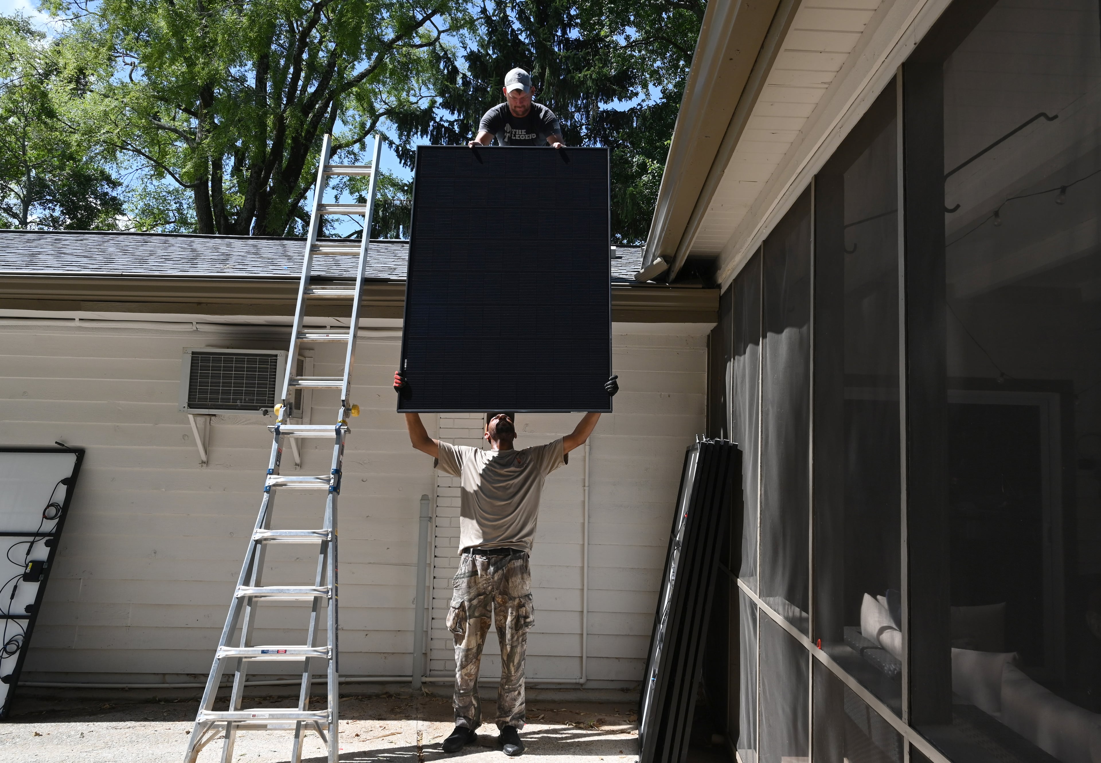 Lionel Carter (bottom) lifts up a solar panel for Ryan Johnson, both with Custom Solar Solutions, as they install solar panels on the roof of an Atlanta area home on Thursday, July 17, 2025. (Hyosub Shin/AJC)
