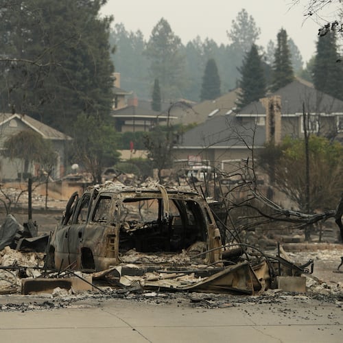 A vehicle and structure are burned on N. Skyline Dr. due to a wildfire, Sunday, Aug. 2, 2026, in Spokane, Wash. (AP Photo/Young Kwak)