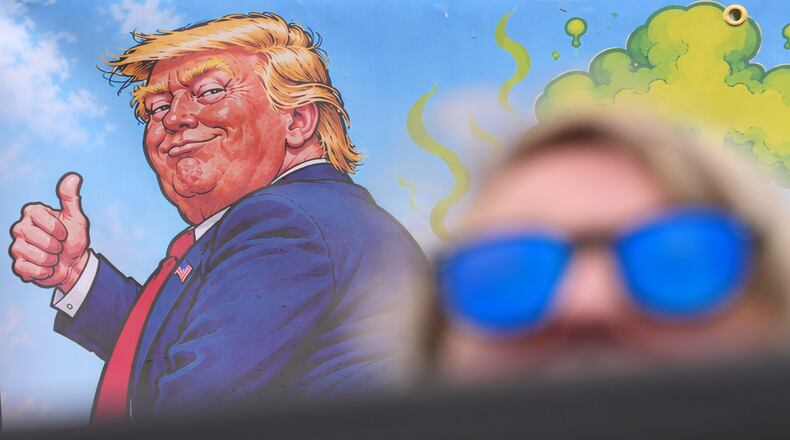 A protester wears sunglasses and sits in front of a poster depicting U.S. President Donald Trump during his visit to the Irish Open at the Trump International Golf Links course in Doonbeg, Ireland, Sunday, Sept. 13, 2026.(AP Photo/Kin Cheung)
