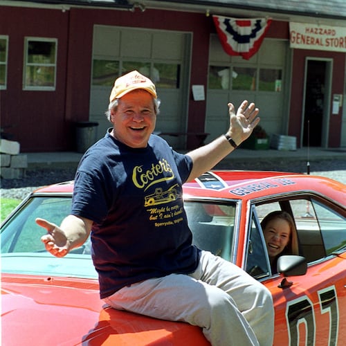 FILE - Cooter, actor Ben Jones, sits atop one of the 229 hotrods, named the General Lee, used in the show "Dukes of Hazzard" as ecstatic fan, Aliceson Johnson, of Charlottesville, Va., sits in the drivers seat in front of his store in Sperryville, Va., Tuesday, Aug. 10, 1999. (AP Photo/Steve Helber, File)