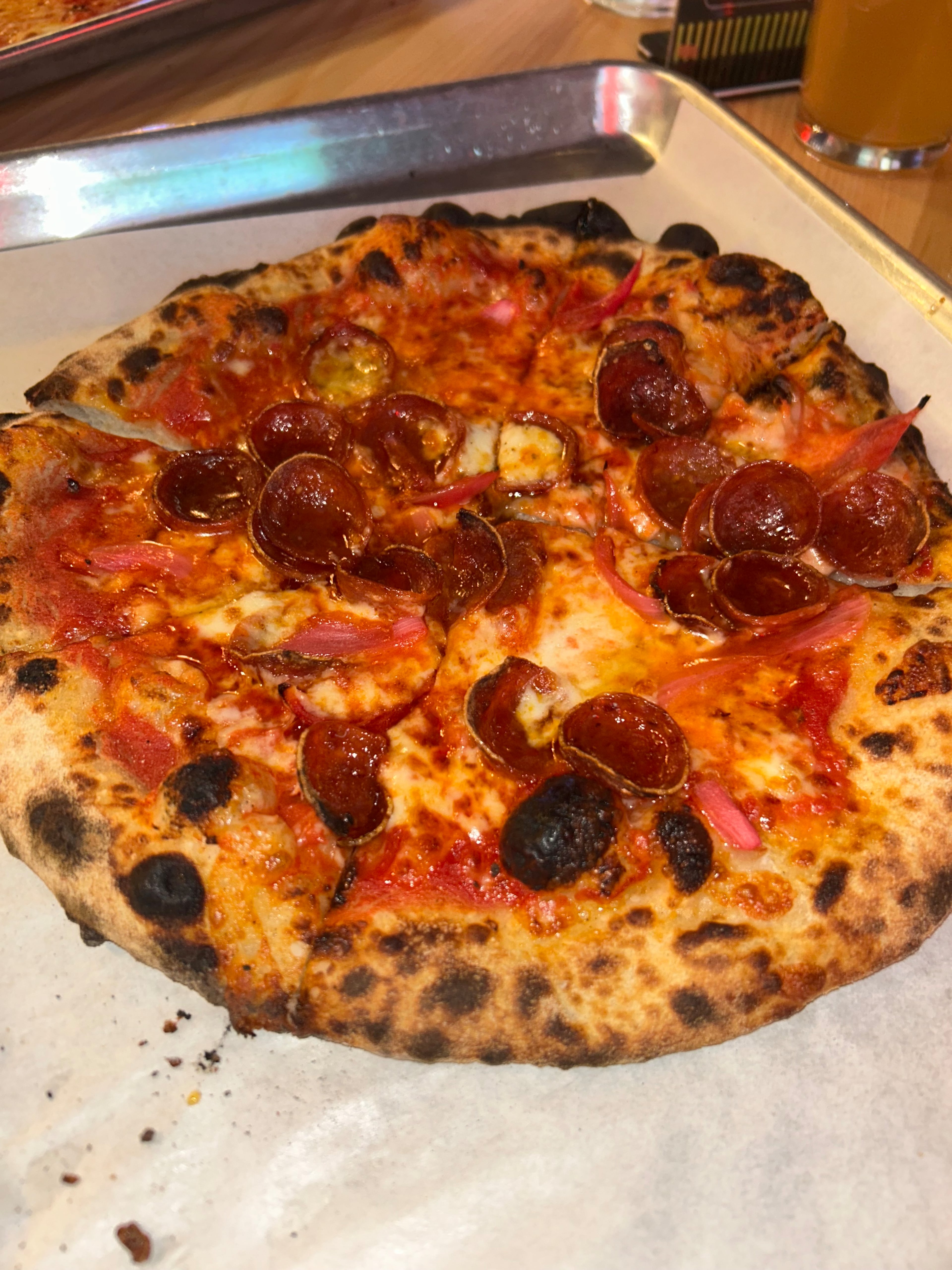 The hot honey pizza at Monday Night Brewing is topped with pepperoni, pickled onions and hot honey for a savory, sweet and acidic combination. The wood-fired oven creates a charred, chewy texture on the crust. (Olivia Wakim/AJC)