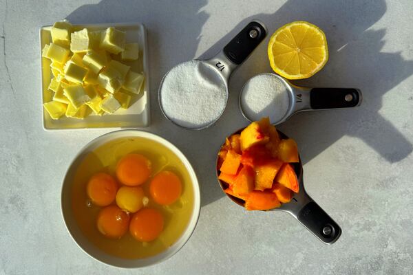 An overhead look at the ingredients used to make peach curd: butter, sugar, lemon, peaches, and eggs.