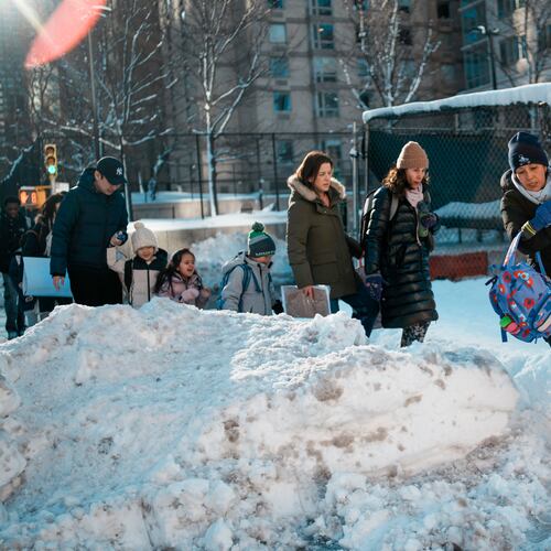 A woman carries a child over piles of plowed snow as she walks a girl to school, Tuesday, Feb. 24, 2026, in New York. (AP Photo/Eduardo Munoz Alvarez)
