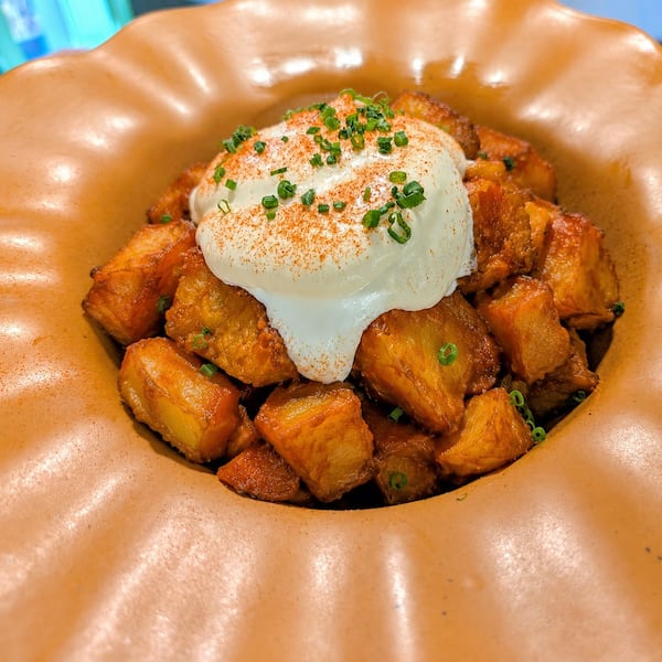 A close-up view of a shallow serving bowl with an oversized rim. In the bowl are fried potatoes dolloped with a creamy topping and garnished with chopped chives.