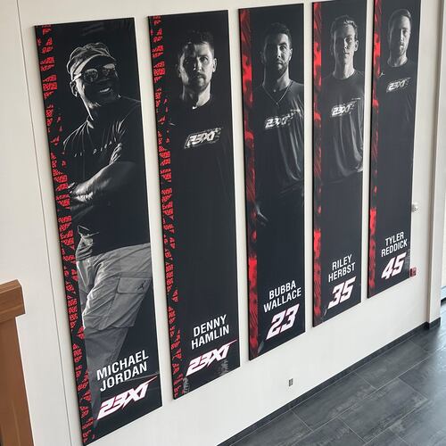 A banner, showing co-owners Michael Jordan and Denny Hamlin, as well as drivers Bubba Wallace, Corey Heim and Tyler Reddick, hangs in the lobby at Airspeed, the headquarters of 23XI Racing, Tuesday, Feb. 24, 2026 in Huntersville, N.C. (AP Photo/Jenna Fryer)