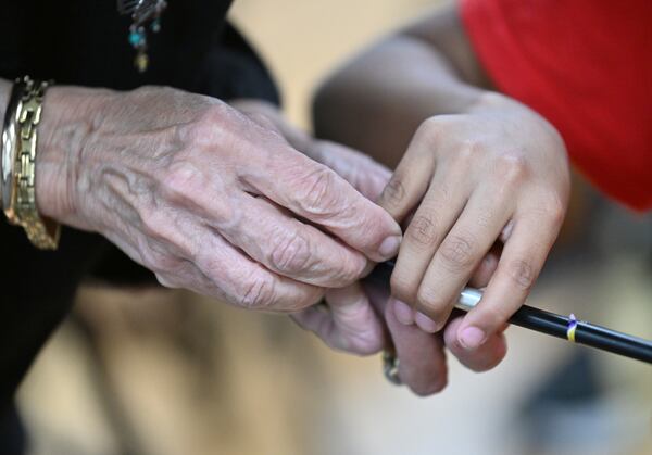 In 2012, music teacher Juana Alzaga, pictured in November helping an orchestra member with holding a violin bow the proper way, was diagnosed with a neuromuscular disease. Of her various health struggles, Alzaga, 71, said: “When I have my down days, I look at the kids, I come here and say, 'I gotta go on.'" (Hyosub Shin/AJC)