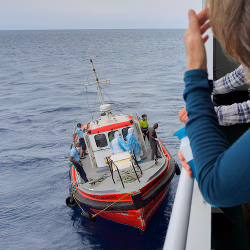 Passengers on the the hantavirus-stricken cruise ship, MV Hondius, watch epidemiologists board the boat in Praia, during their voyage to Spain's port of Tenerife, May 6, 2026. (AP Photo)