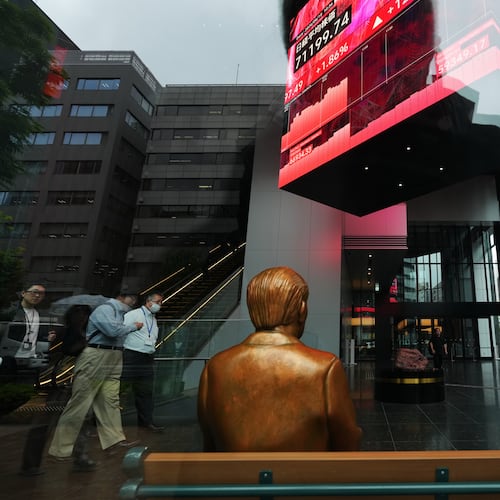 A statue is placed on a bench near monitors showing Japan's Nikkei 225 index, hanging in a business building in Tokyo, Thursday, June 18, 2026. (AP Photo/Hiro Komae)