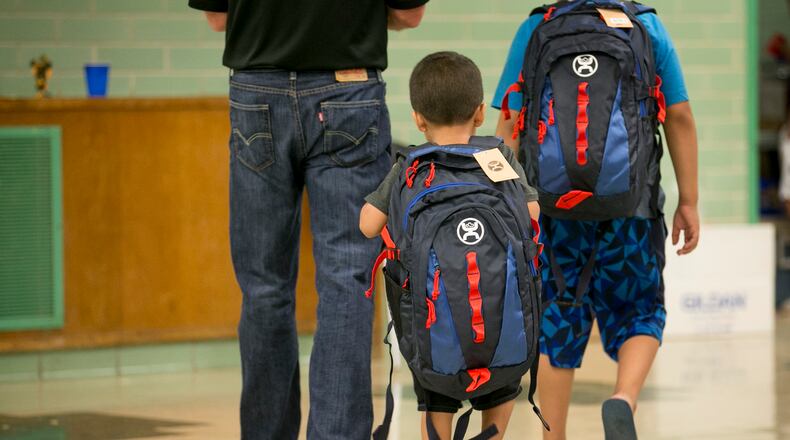 Adrien Sosa, 4, middle, and his brother Eric Sosa, 8, walk away with new backpacks filled with new clothes and books  at the Manos de Cristo Back-to-School Program at the Allan Early Childhood Center on Tuesday July 25, 2017.  The nonprofit Manos de Cristo is providing the school supplies and clothes to children, aged pre-K to 5th grade, every morning this week.   Hundreds of volunteers, including board member Paul Miller, left, will serve 2,000 children with  supplies which were donated by corporate sponsors and individuals.  JAY JANNER / AMERICAN-STATESMAN
