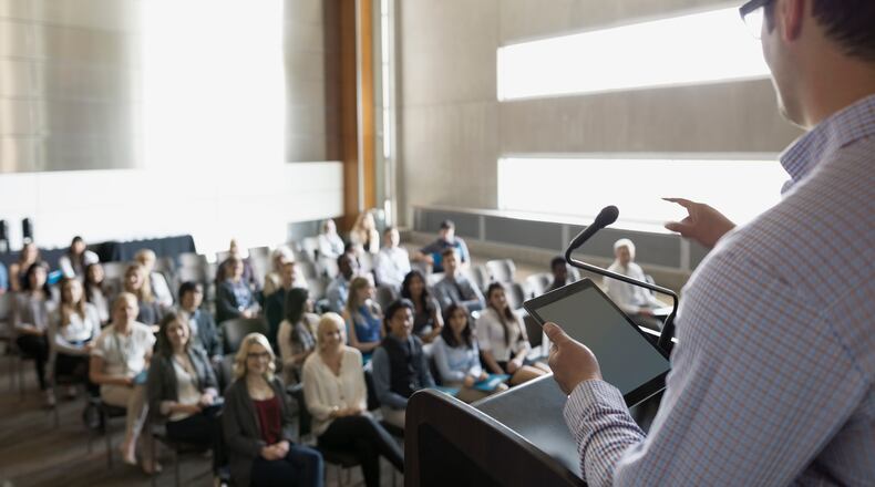 Professor with digital tablet speaking to students in auditorium (stock photo)