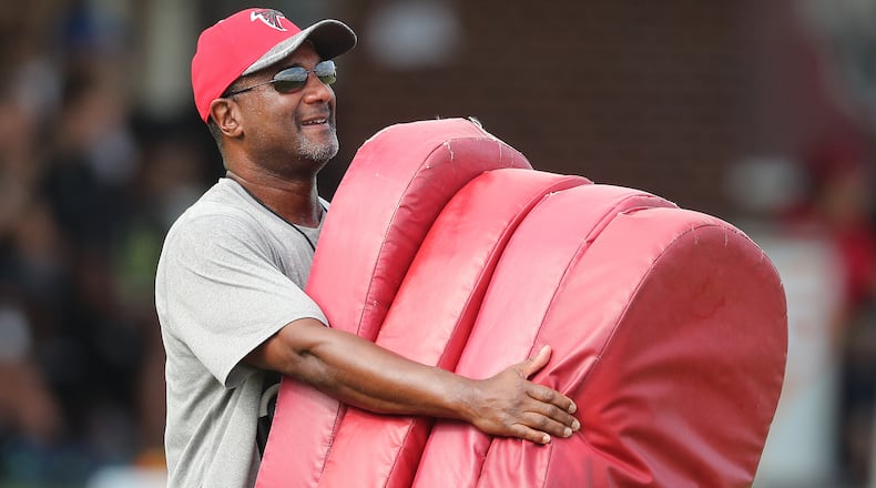 Falcons special teams coordinator Keith Armstrong carries some blocking pads out to the field for the first day of training camp on Thursday, July 28, 2016, in Flowery Branch.