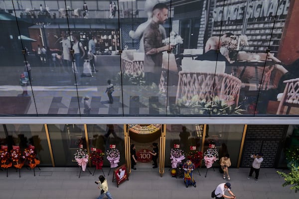 Workers wait for customer at a jewellry store as a projector screen promoting a newly opened outdoor Hutong style shopping mall, in Beijing, Monday, May 26, 2025. (AP Photo/Andy Wong)
