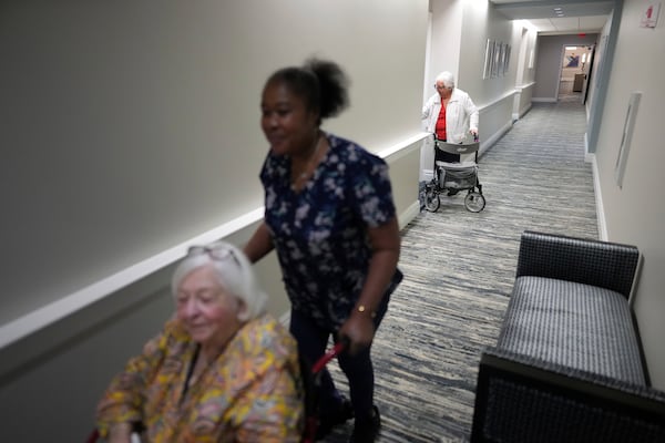 Private nursing assistant Mona Dagobert, center, pushes Eleanor Kirshner, 86, to her apartment after saying goodbye to friend Isa Medow, top, in the independent living facility at the Toby and Leon Cooperman Sinai Residences, July 4, 2025, in Boca Raton, Fla. (AP Photo/Rebecca Blackwell)