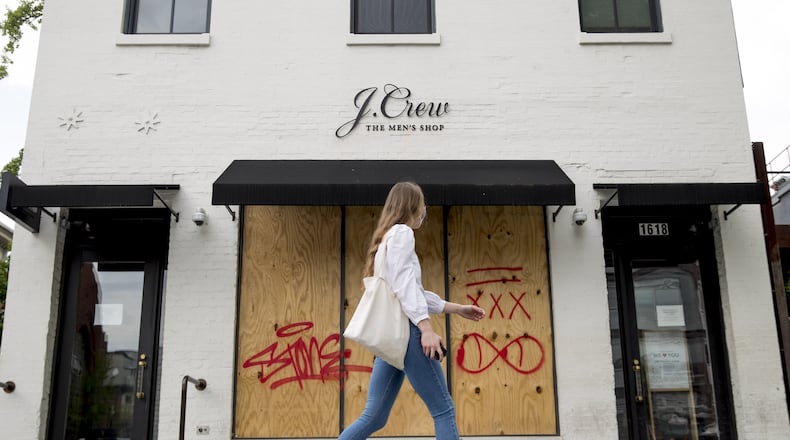 In this April 29, 2020, file photo, a woman walks past a boarded up J. Crew storefront along 14th Street in Northwest Washington. The parent company of clothing chain J. Crew has filed for Chapter 11 bankruptcy, yet another casualty of the coronavirus pandemic. (AP Photo/Andrew Harnik, File)