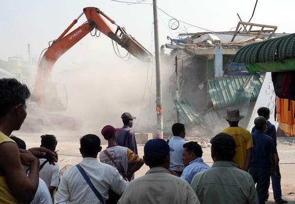 People watch as a backhoe clear debris from damaged buildings at a market, after one month of the strong earthquake in Naypyitaw, Myanmar, Monday, April 28, 2025. (AP Photo/Aung Shine Oo)