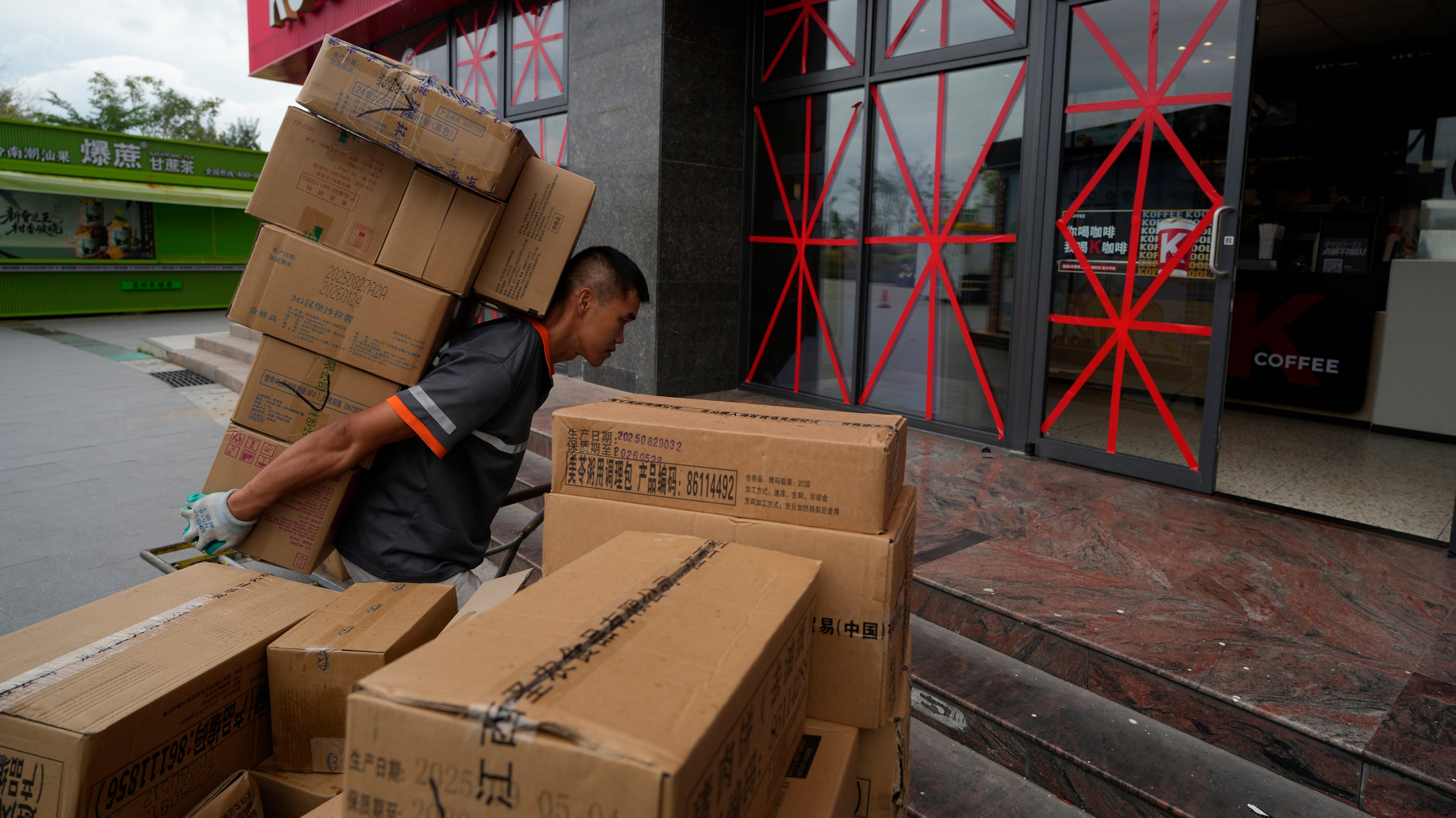 A delivery man carries goods into a restaurant with its windows taped protectively against strong winds ahead of Super Typhoon Ragasa in Shenzhen in southern China's Guangdong province on Tuesday, Sept. 23, 2025. (AP Photo/Ng Han Guan)