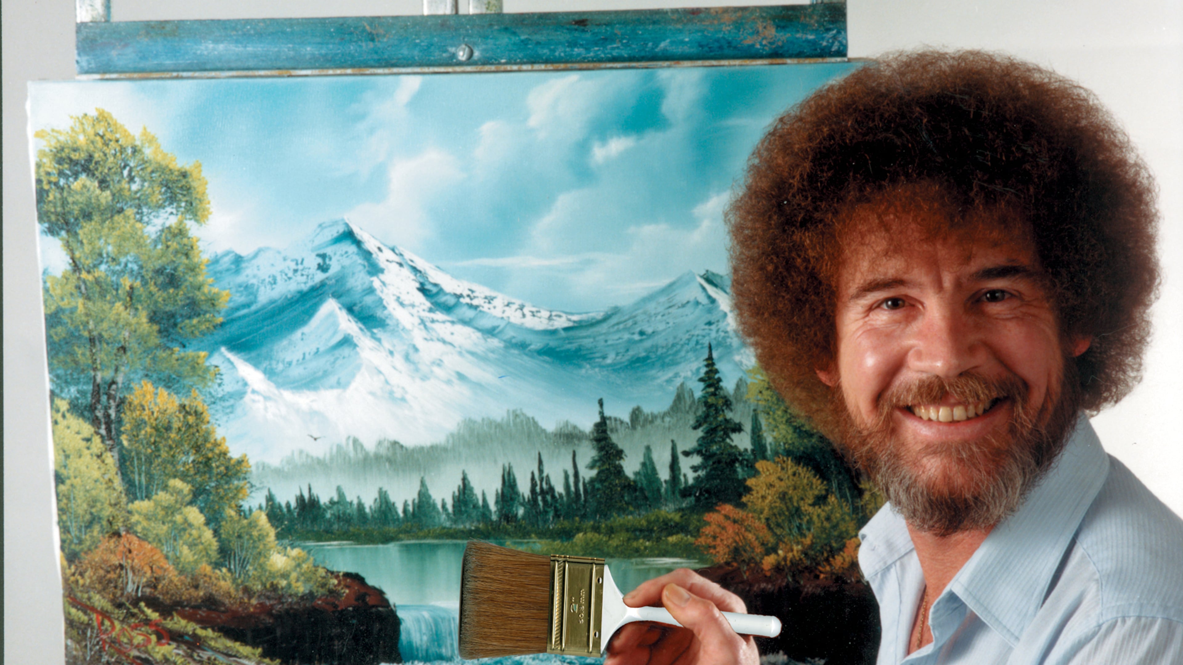 In this undated photo provided by Bob Ross Inc., Bob Ross poses for a photo in front of one of his paintings. (Bob Ross Inc. via AP)
