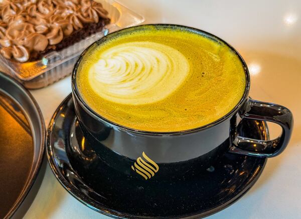 An artfully poured latte in a black mug sits on a saucer on a table in a coffee shop.
