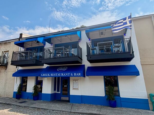 The exterior of a new Greek restaurant called Limani in with blue marquee shades over the door and windows and Greek flags over the balconies.
