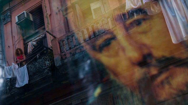 FILE - A Cuban woman hanging laundry on her balcony is seen reflected in a glass window decorated with a poster of Cuba's leader Fidel Castro in Old Havana, Cuba, Thursday, Dec. 27, 2007. (AP Photo/Dado Galdieri, File)